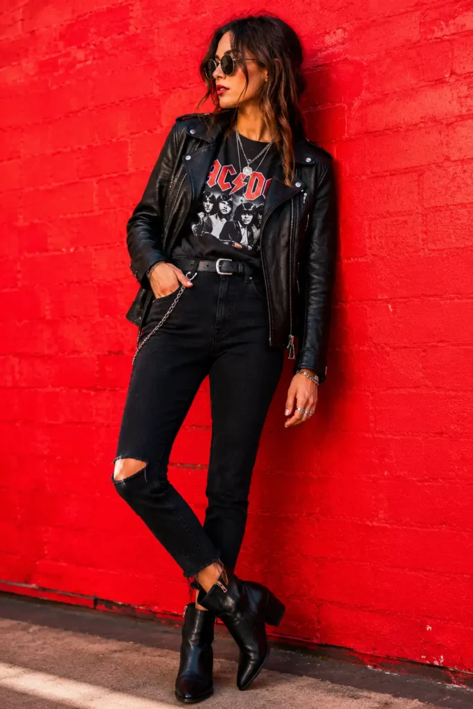 Femme en look rock moderne avec perfecto noir, jean noir et bottines cuir devant un mur rouge vif.