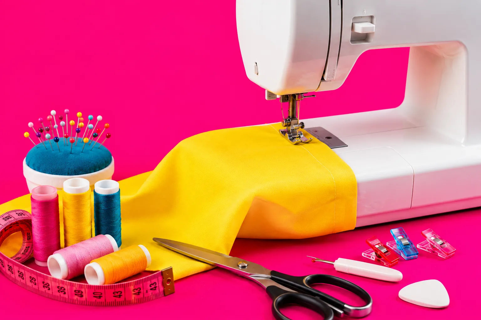Machine à coudre avec tissu jaune et accessoires couture sur fond rose flashy